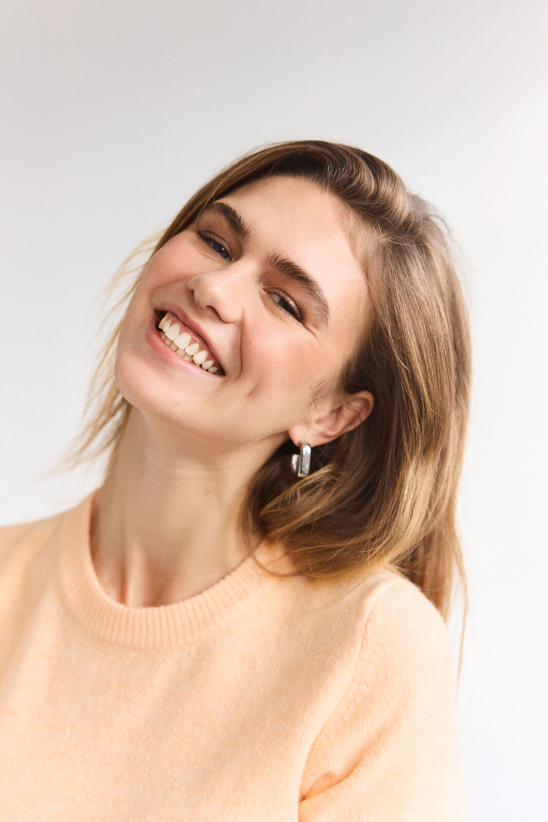 Model smiling wearing a orange pastel pullover