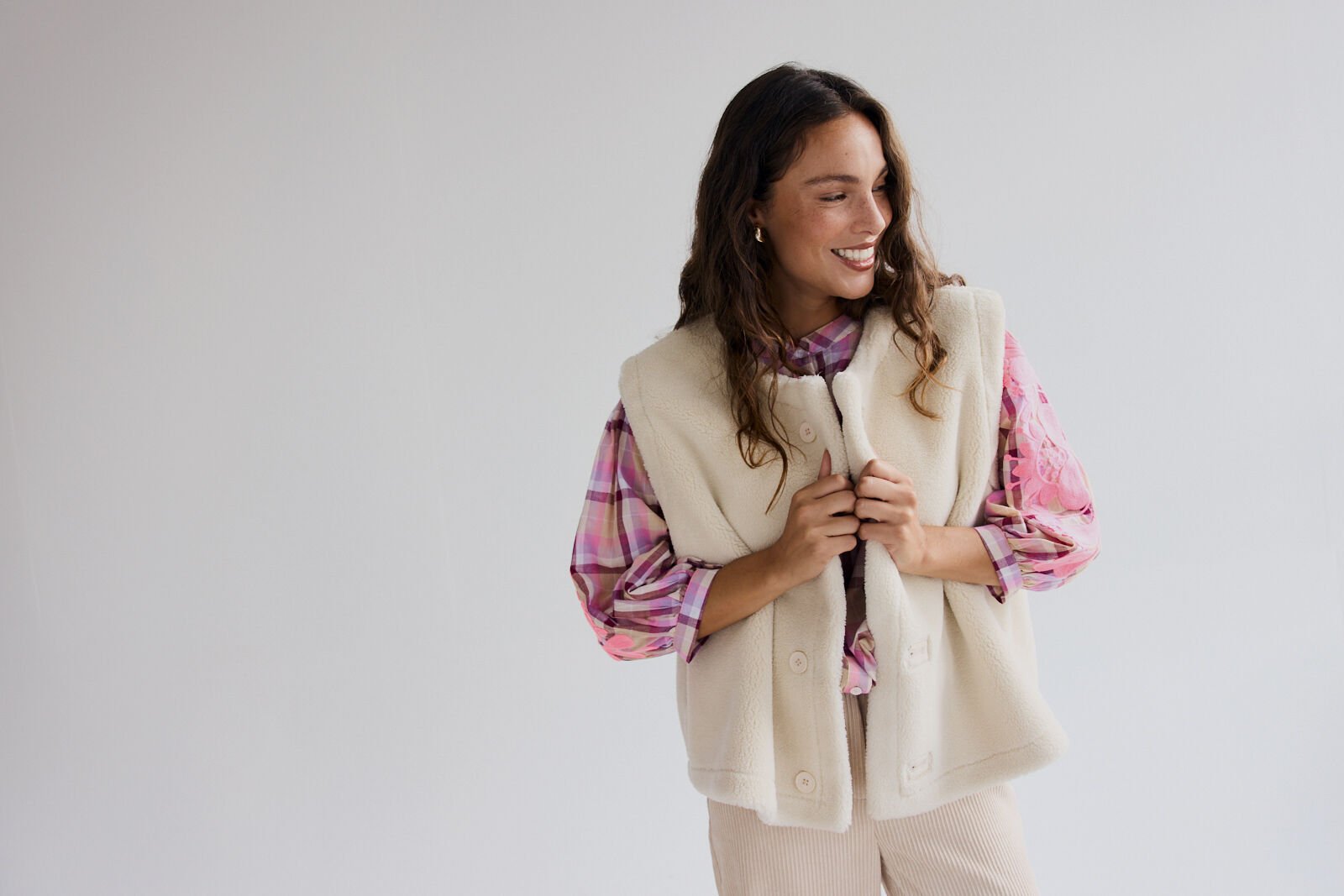 Two women collaborate at a design table covered with fabric swatches, sketches, and sewing tools in a bright studio.